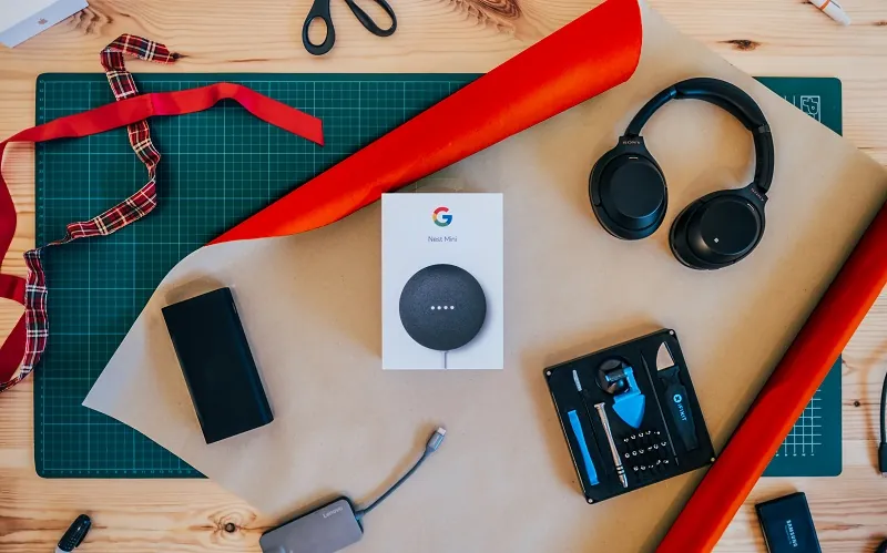 Stor bild med bord med presentpapper, Google Home Mini och hörlurar.